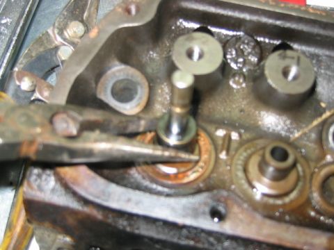 1992 Ford Bronco - Close-up of a cylinder head or engine block casting showing a valve assembly, with pliers gripping a valve spring retainer or keeper during…
