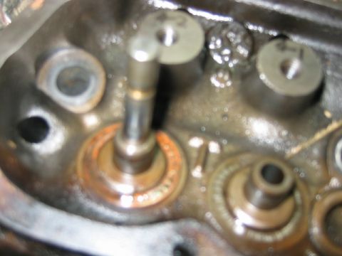 1992 Ford Bronco - Close-up of a cylinder head with a valve spring removed, showing the exposed valve stem protruding through the guide and an adjacent valve…