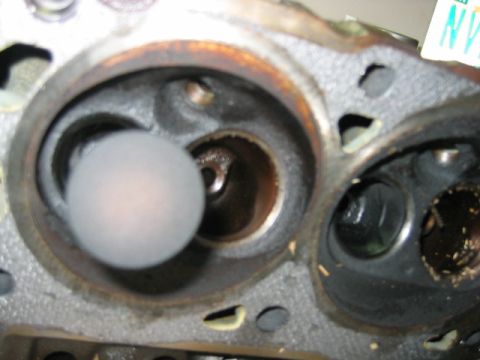 1992 Ford Bronco - Close-up of a cylinder head combustion chamber showing intake and exhaust valves, with a round plastic cap or plug covering one port. The m…