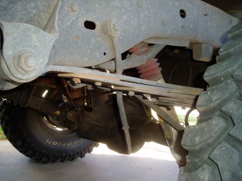 1990 Ford Bronco - Underbody shot of a lifted 4x4's rear suspension showing the leaf-spring pack, sway-bar link and frame bracket, with a red-boot shock and t…