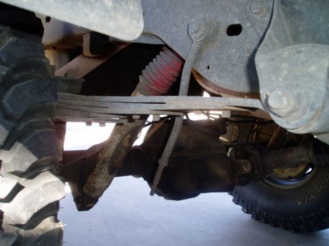 1990 Ford Bronco - Underbody view of a lifted truck's rear leaf-sprung axle, with a red-boot shock, driveshaft and U-joint, and a yellow-painted axle housing…