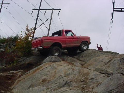 1978 Ford Bronco - A red 1978 Ford Bronco navigates a challenging rocky terrain under a cloudy sky.