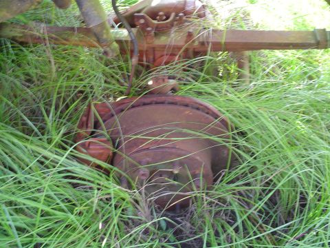 1984 Chevrolet Blazer - A rusty brake rotor and axle assembly sits in tall grass, suggesting a vehicle part removed from service.