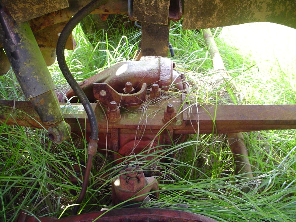 close-up of a rusty rear axle assembly with grass growing around it