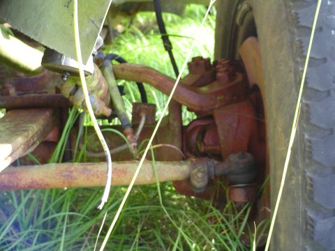 1984 Chevrolet Blazer - Close-up view of a vehicle's undercarriage, showing rusted suspension parts amidst tall grass.