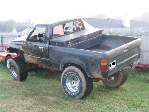 1986 Ford F-150 - This black Toyota pickup truck has a toolbox mounted in the bed and is parked on a grassy area.