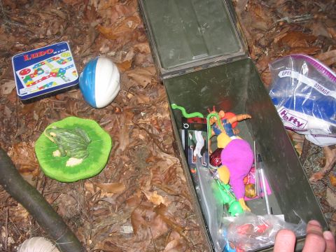1988 Ford Bronco - Contents of a geocache, including toys and games, are laid out on the forest floor.