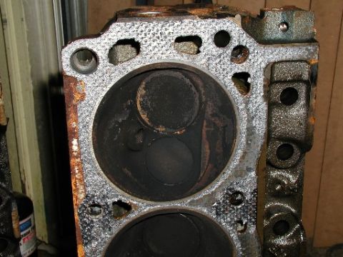 1990 Ford Bronco - Close-up of an engine cylinder head showing the combustion chambers and valves, with visible carbon deposits.