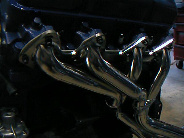 Polished tubular exhaust headers bolted to an engine block in a shop