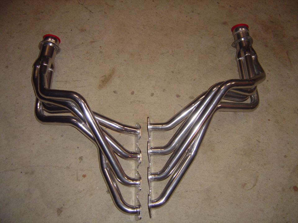 Pair of polished stainless V8 long-tube headers with red collector caps on concrete