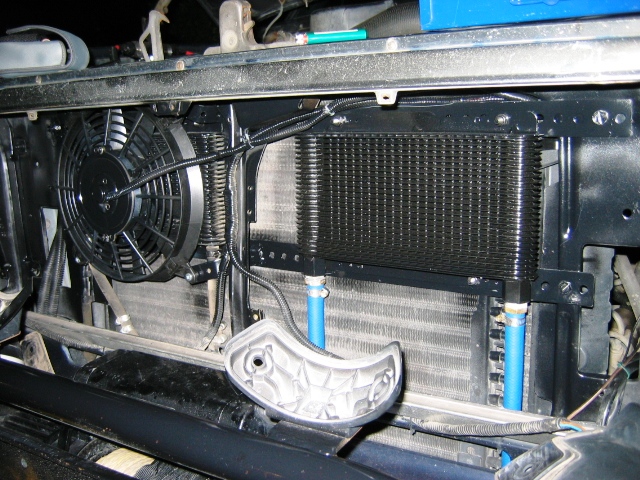 Electric fan and aluminum radiator with finned cooler and blue fittings behind vehicle grille