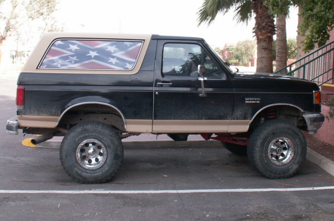 Black lifted two-door Ford Bronco SUV in side view with Confederate flag on hardtop