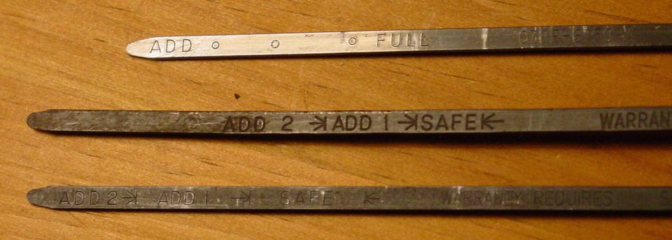 Three metal dipsticks on wood, stamped ADD, FULL, SAFE and warranty text