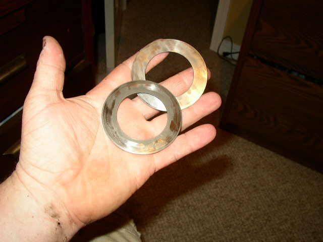 Two worn metal rings with brown discoloration held in a palm, with a wooden dresser in the background