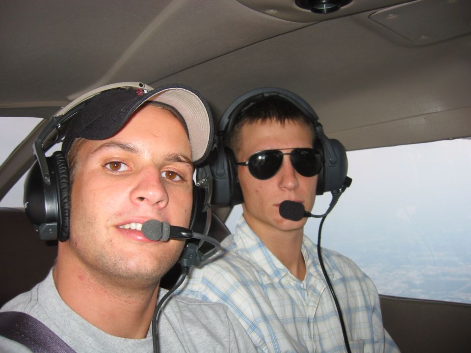 Two young men wearing aviation headsets inside a small aircraft cockpit