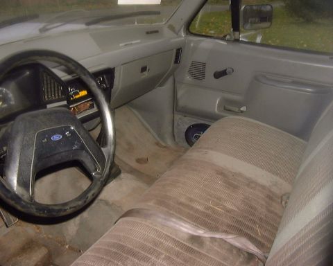 1985 Ford F-150 - The interior of a 1985 Ford F-150 shows tan striped seats, a dashboard with gauges, and a Ford steering wheel.
