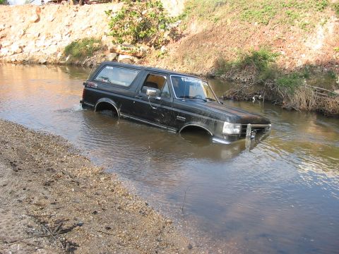 1988 Ford Bronco - This black SUV is partially submerged in a shallow creek, with water reaching its windowsills.