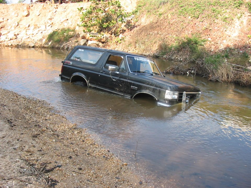 Black Ford Bronco fording a creek with water at the door sills, front 3/4 view