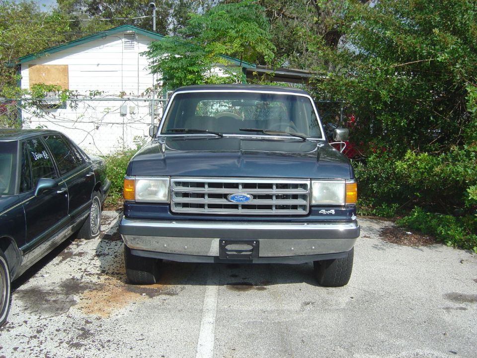 Dark blue Ford Bronco with chrome grille and bumper, parked next to a sedan