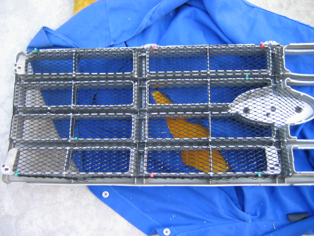 Black mesh grille panel with oval bolt plate resting on blue fabric
