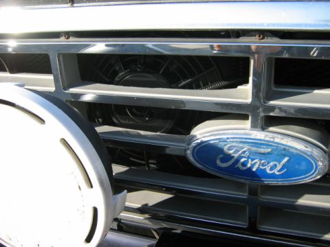 1985 Ford Bronco - Close-up of the 1985 Ford Bronco's grille, the iconic blue oval Ford badge and a visible cooling fan.