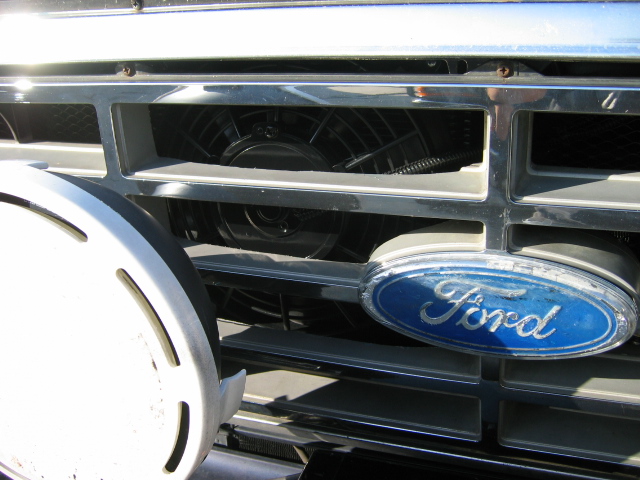Close-up of chrome Ford grille with blue oval emblem and visible fan behind slats
