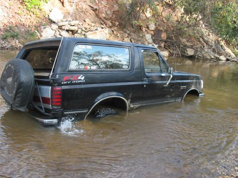 1988 Ford Bronco - A black Ford Bronco is partially submerged in a shallow body of water, with the FX4 off-road decal visible on the side.