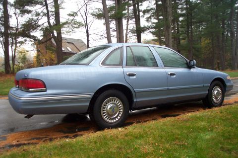 1991 Ford Crown Victoria LTD - A light blue sedan is parked on the side of a road with trees in the background.