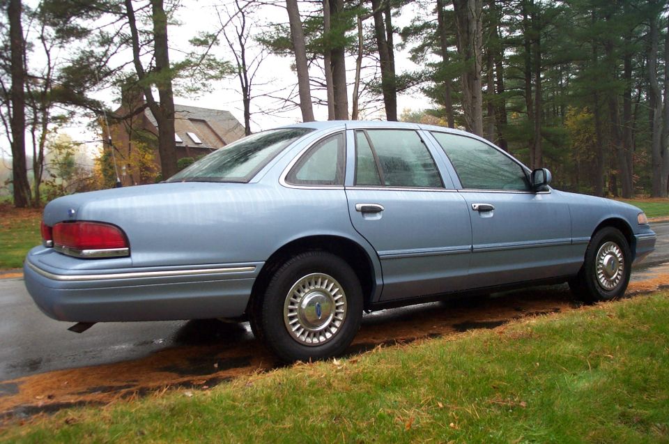 Light blue sedan parked on a wet road, side view. The car has chrome trim and hubcaps