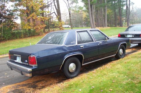 1991 Ford Crown Victoria LTD - A dark blue 1980s Ford Crown Victoria is parked on the side of the road with fall foliage in the background.
