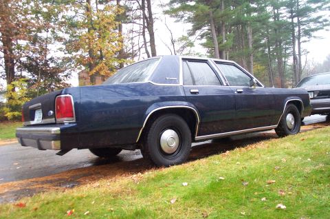 1991 Ford Crown Victoria LTD - A dark blue sedan with chrome trim sits parked on a grassy area next to a road.