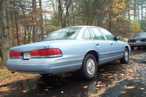 1991 Ford Crown Victoria LTD - A light blue sedan is parked on a wet surface with autumn leaves scattered around.