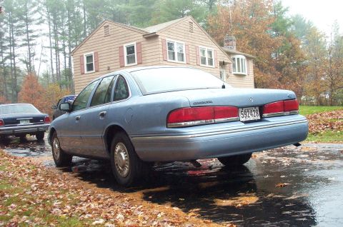 1991 Ford Crown Victoria LTD - A light blue 1991 Ford Crown Victoria LTD is parked in front of a house on a wet, leaf-covered driveway.