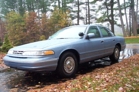 1991 Ford Crown Victoria LTD - A 1991 Ford Crown Victoria LTD is parked outdoors on a damp day with autumn foliage in the background.