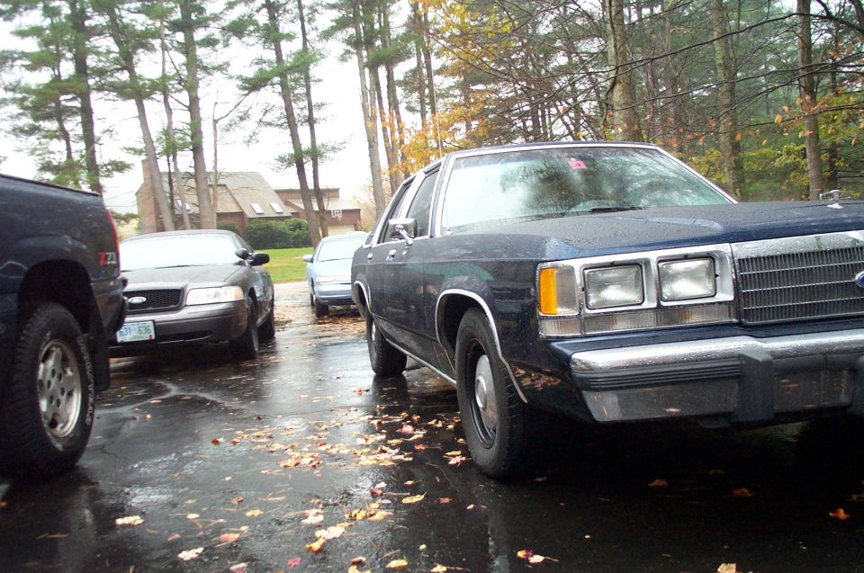 Dark blue sedan with chrome grille and rectangular headlights parked next to a black pickup truck