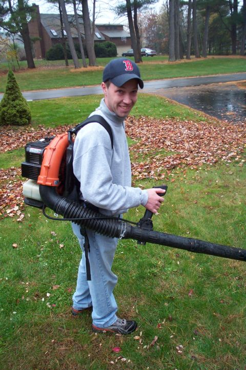 1991 Ford Crown Victoria LTD - Man with a backpack leaf blower on a lawn with fallen leaves and trees in the background.