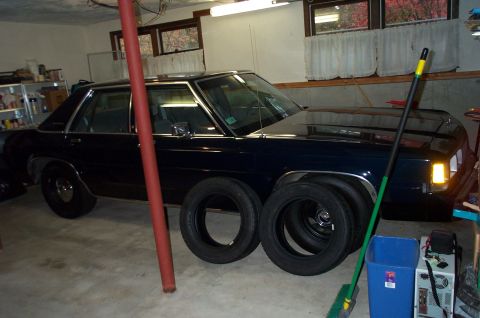 1991 Ford Crown Victoria LTD - A dark blue sedan is parked in a garage, with spare tires placed next to it.