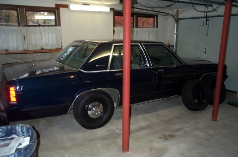 1991 Ford Crown Victoria LTD - A dark blue sedan with chrome trim and vinyl roof is parked in a garage, showing its side profile.