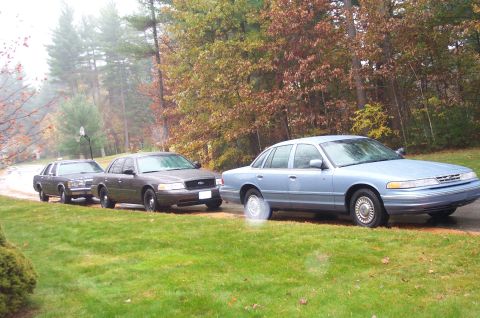 1991 Ford Crown Victoria LTD - Three Ford Crown Victoria LTD sedans are parked on a wet road during autumn. The lead vehicle is light blue, while the two behind it are da…