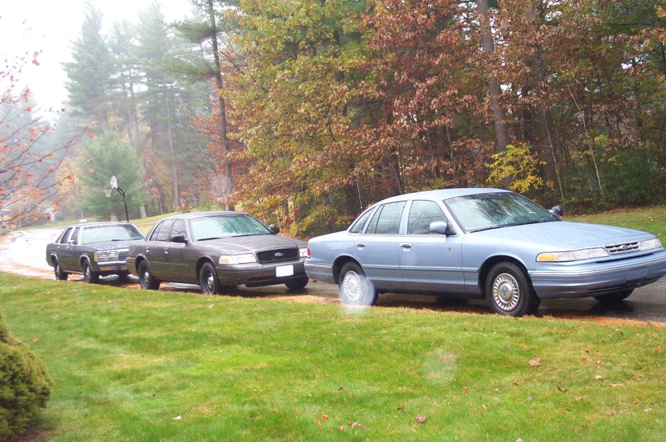 Light blue 1991 Ford Crown Victoria LTD sedan parked on a wet road with two dark sedans behind it