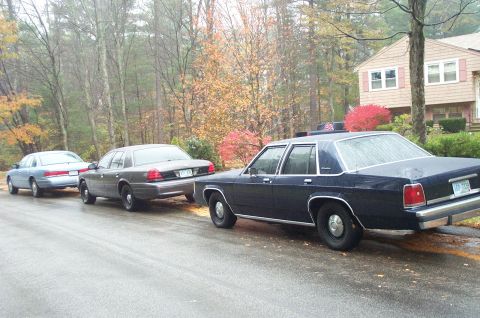 1991 Ford Crown Victoria LTD - Three Ford Crown Victoria police cars are parked on a wet street during autumn. The closest car is dark blue, followed by a gray one, and t…