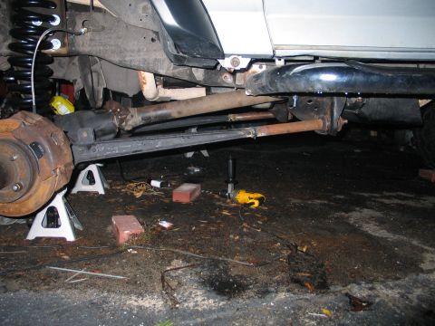 1992 Ford Bronco - Underside view of a vehicle raised on Pro-Lift jack stands, showing the front differential, driveshaft, coil spring, rusty brake rotor and…