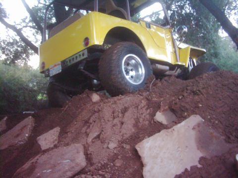 1978 Ford Bronco - Yellow off-road jeep navigates a steep dirt incline with large rocks.