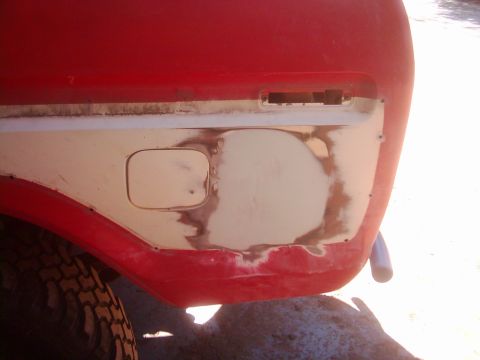 1978 Ford Bronco - The rear quarter panel of a red vehicle shows a fuel door and areas of body filler, indicating repair work.