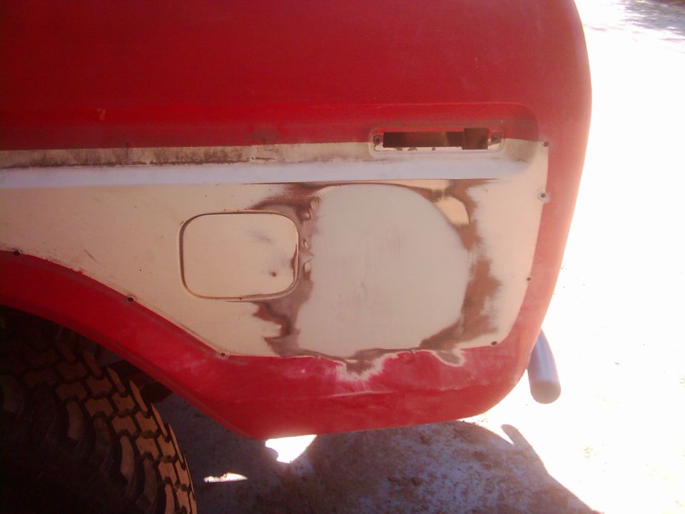 Red vehicle rear quarter panel with a fuel door and body filler