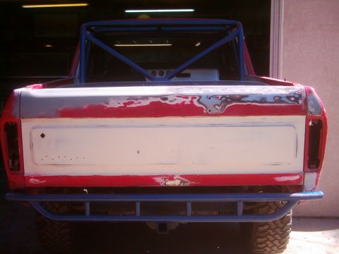 1978 Ford Bronco - Rear view of a 1978 Ford Bronco undergoing bodywork, showing primer and red paint with a blue roll cage and bumper.