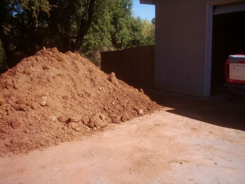 1978 Ford Bronco - A large pile of dirt sits in front of a garage, with the rear of a red and white vehicle visible within the garage opening.