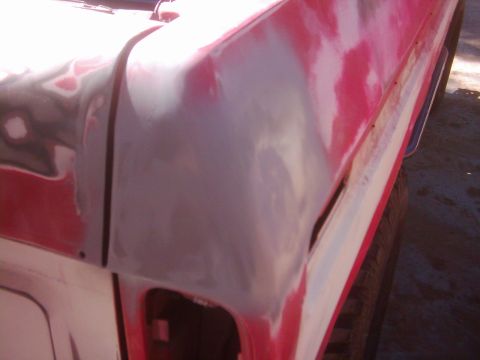 1978 Ford Bronco - Close-up of a red vehicle's body panel undergoing repair, with primer and filler visible.
