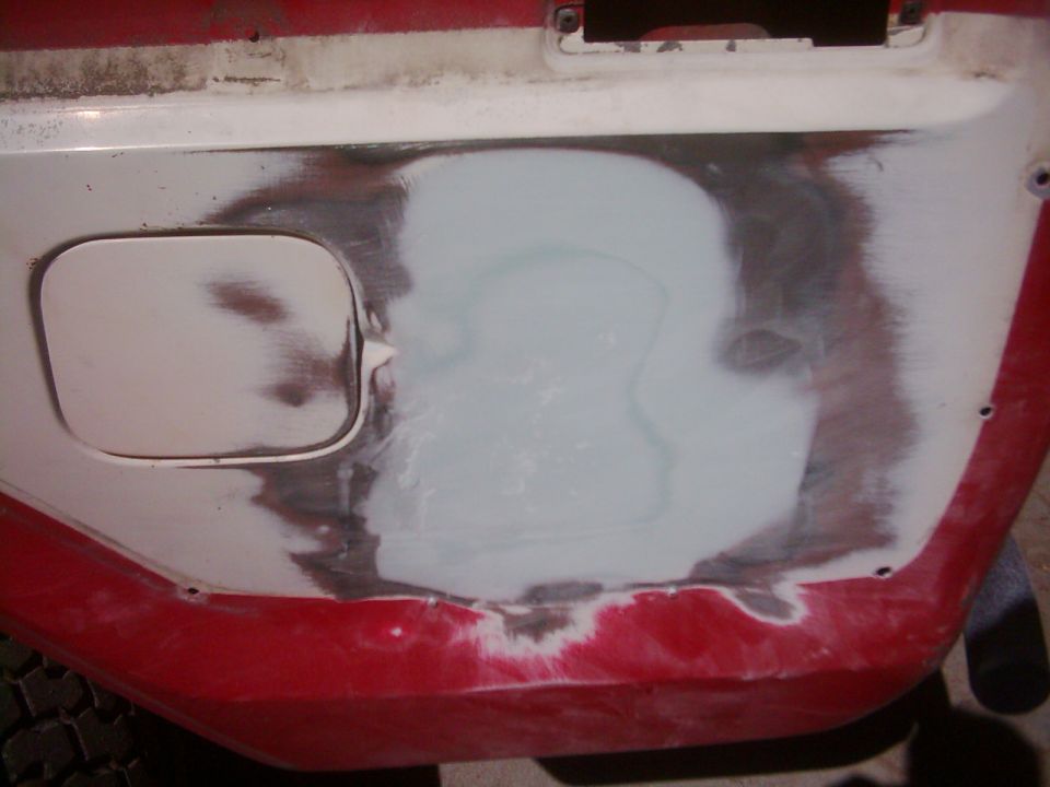 close-up of red vehicle body panel with body filler applied over dented area, fuel door visible