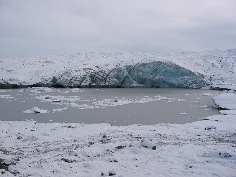 Blue glacier ice meeting a partly frozen lake in a snowy landscape